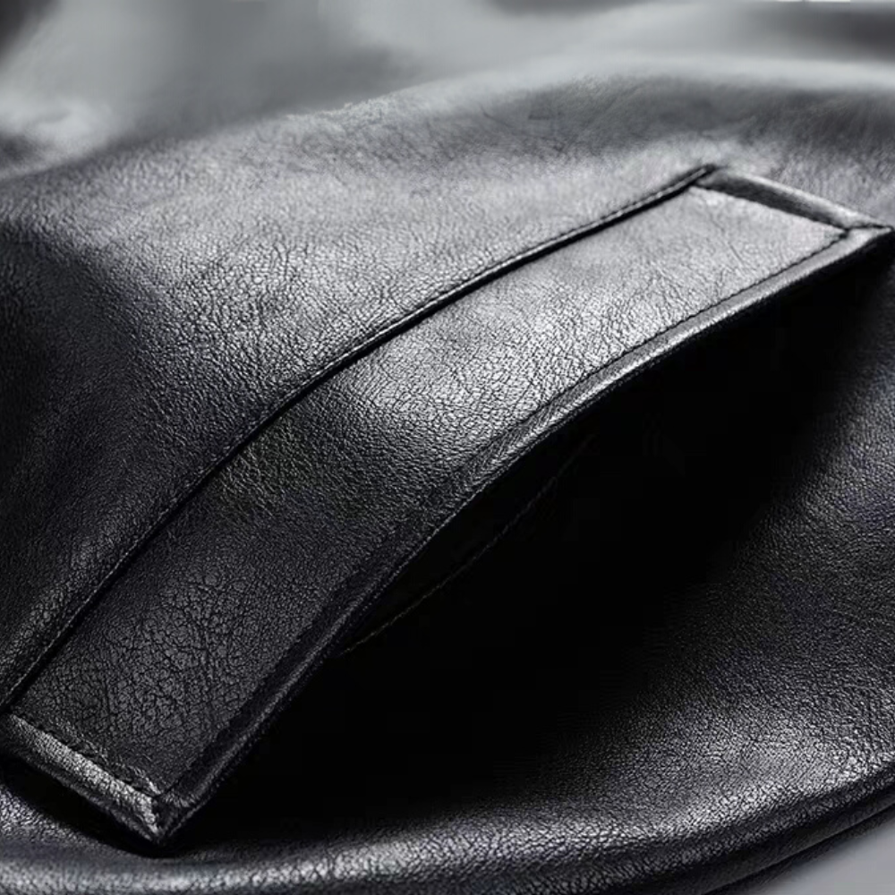 Close-up of side pocket opening on black faux leather varsity jacket, showing stitching and PU texture near hem