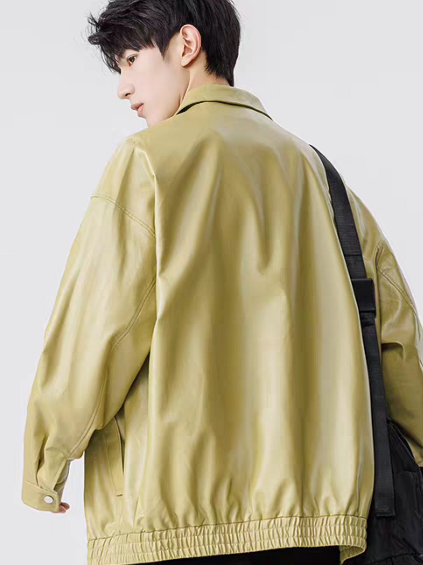 Model wearing green faux leather varsity jacket, shown from back angle with shoulder stitching and elastic hem