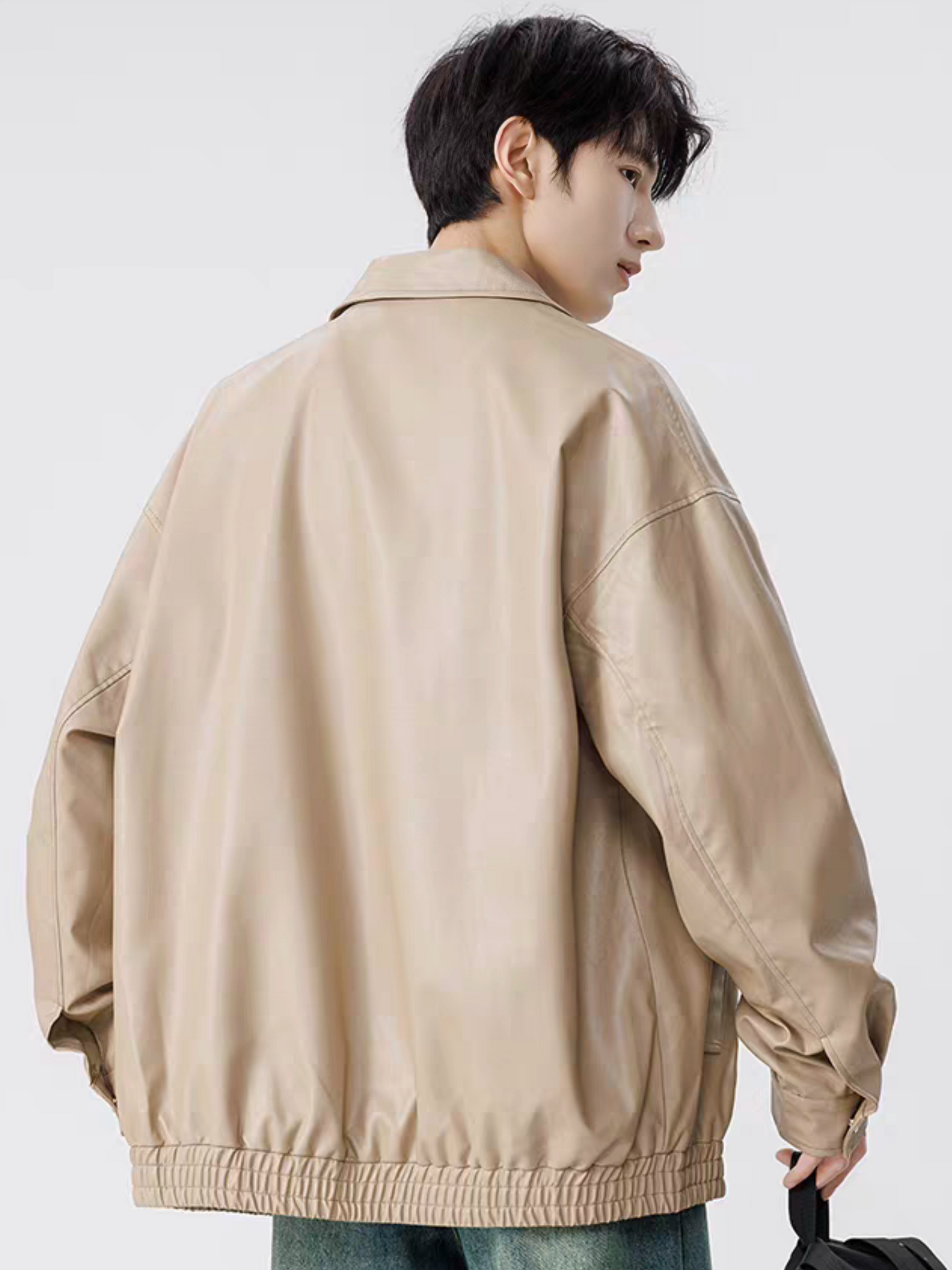 Model wearing khaki faux leather varsity jacket, shown from back angle with drop-shoulder design and elastic hem