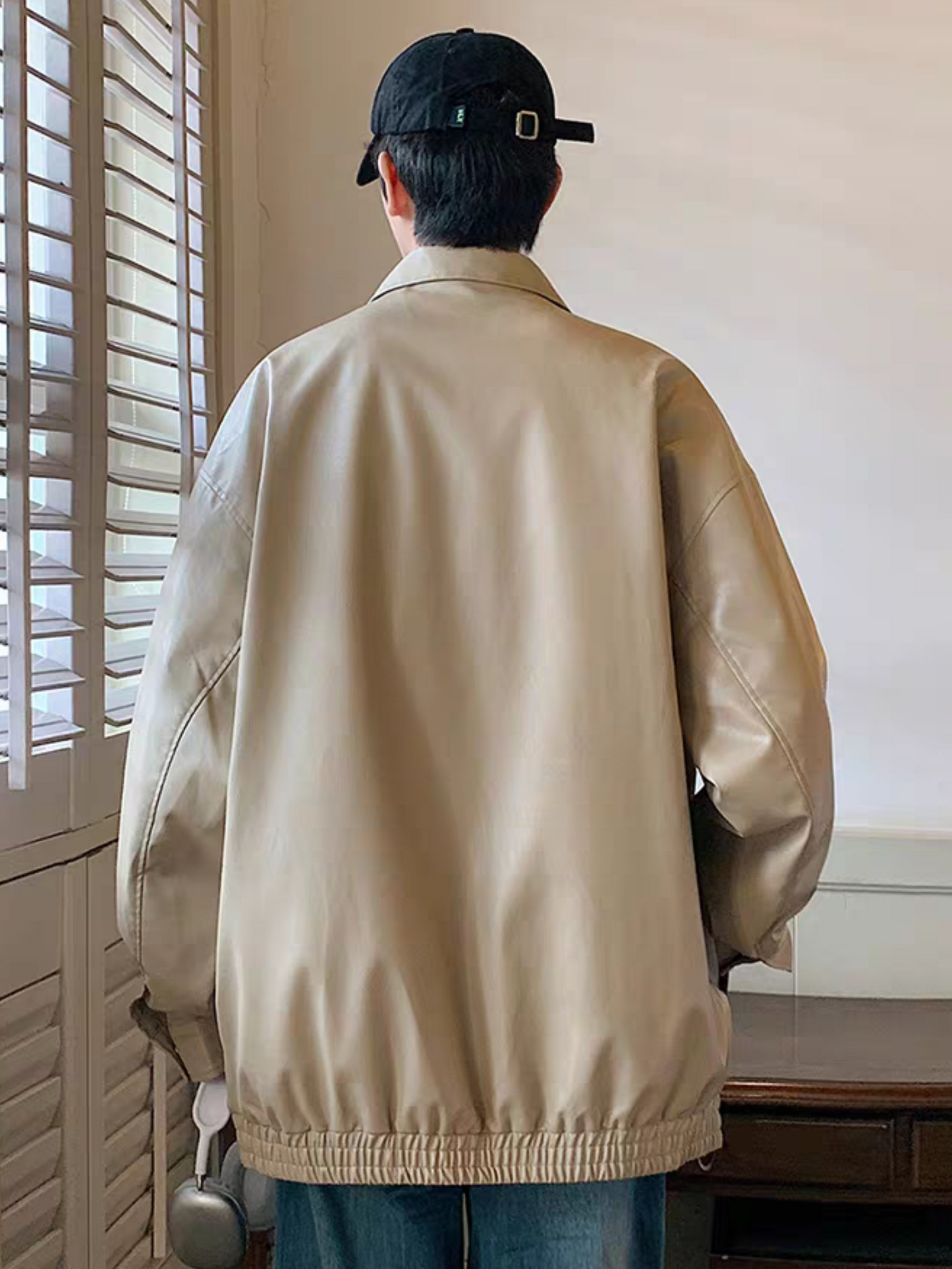 Model wearing khaki faux leather varsity jacket viewed from the back showcasing relaxed fit and matte texture in indoor daylight