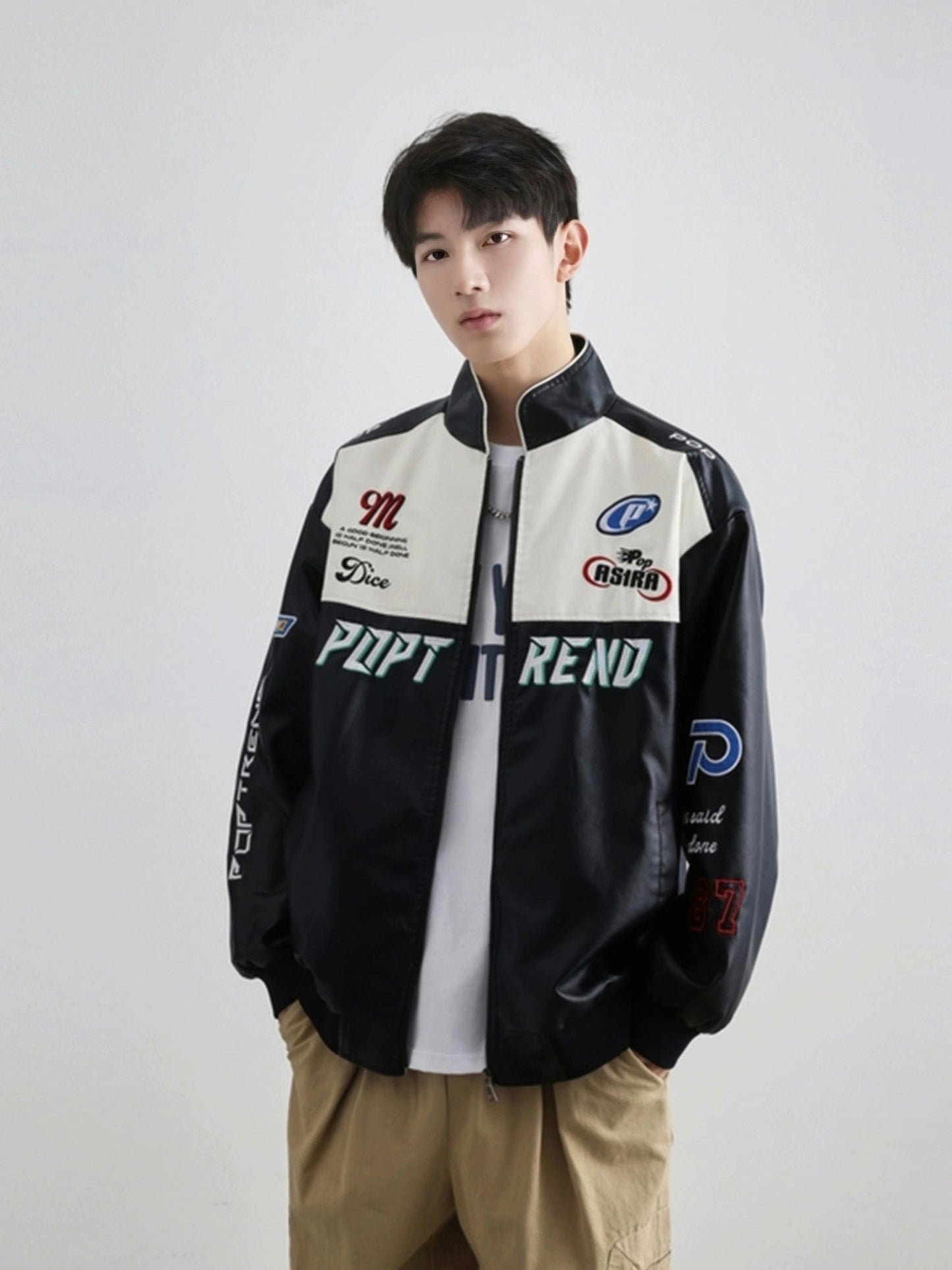 Model front view wearing black PU leather racing jacket with embroidered logos minimalist studio background