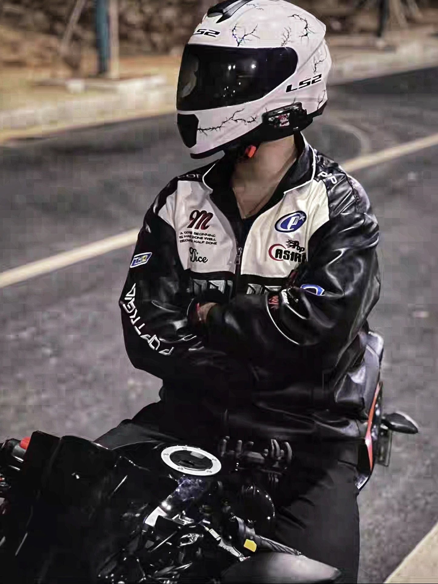 Biker wearing black Pop Trend PU leather racing jacket and helmet, sitting on motorcycle at night