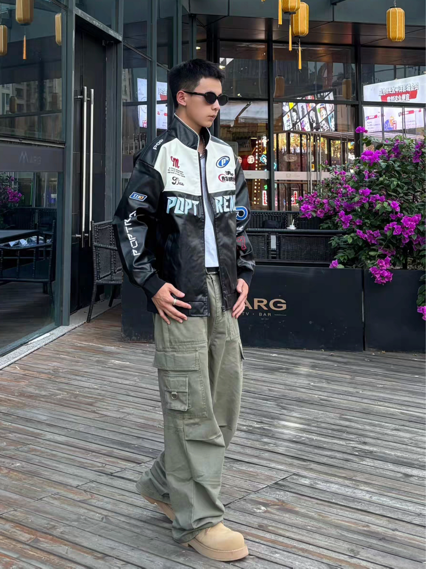 Male model wearing black racing moto jacket with cargo pants, styled in urban outdoor streetwear look