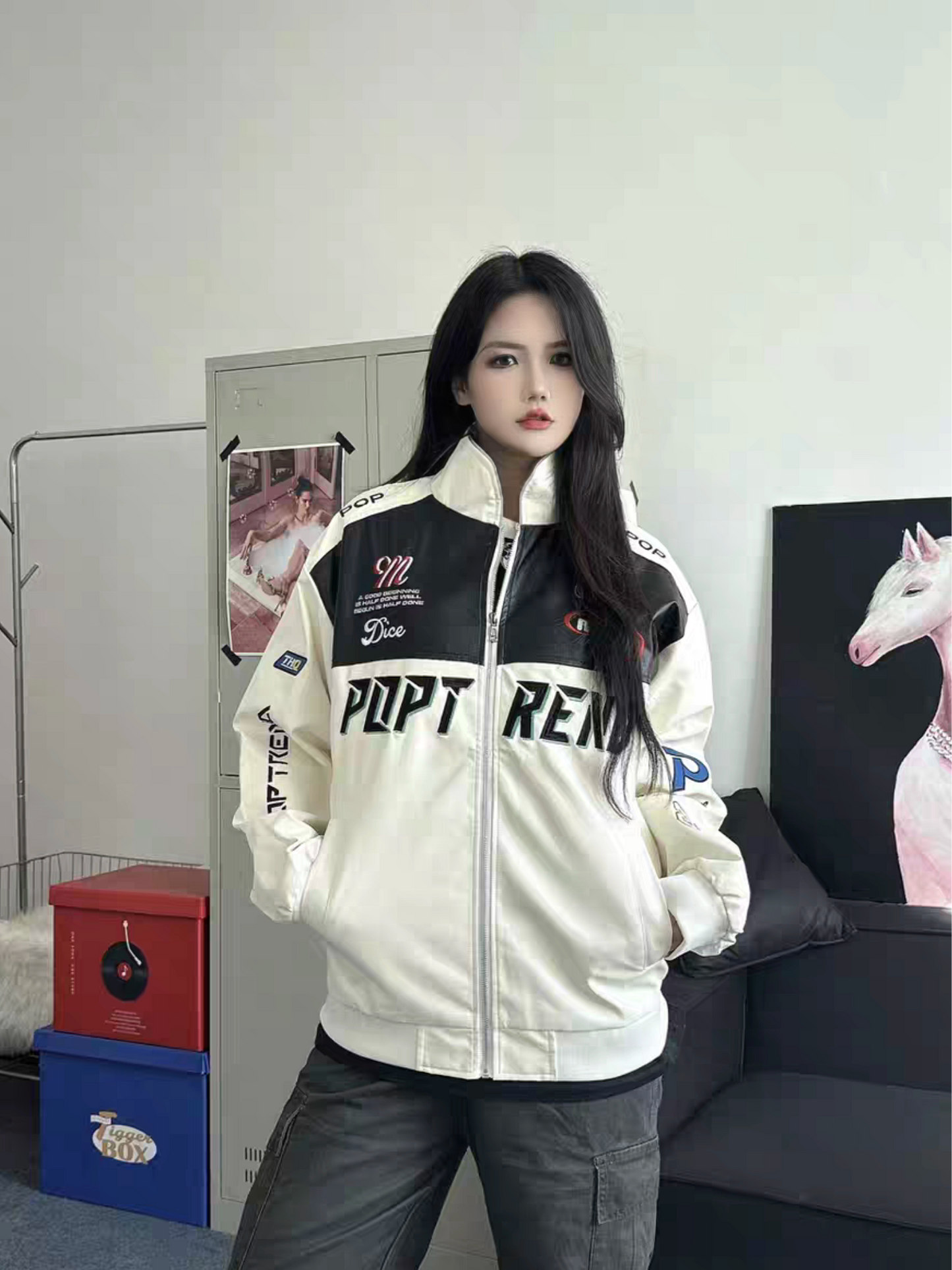 Female model wearing white racing PU leather jacket with hands in pockets, showcasing unisex streetwear style in an indoor casual setting