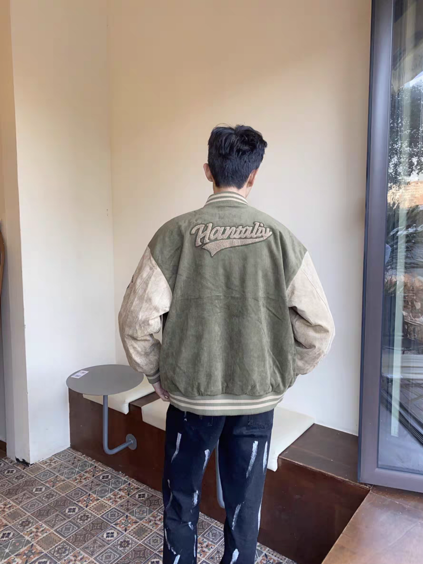 Back view of male model wearing green and brown Hantaliv varsity jacket showing embroidered logo on the back