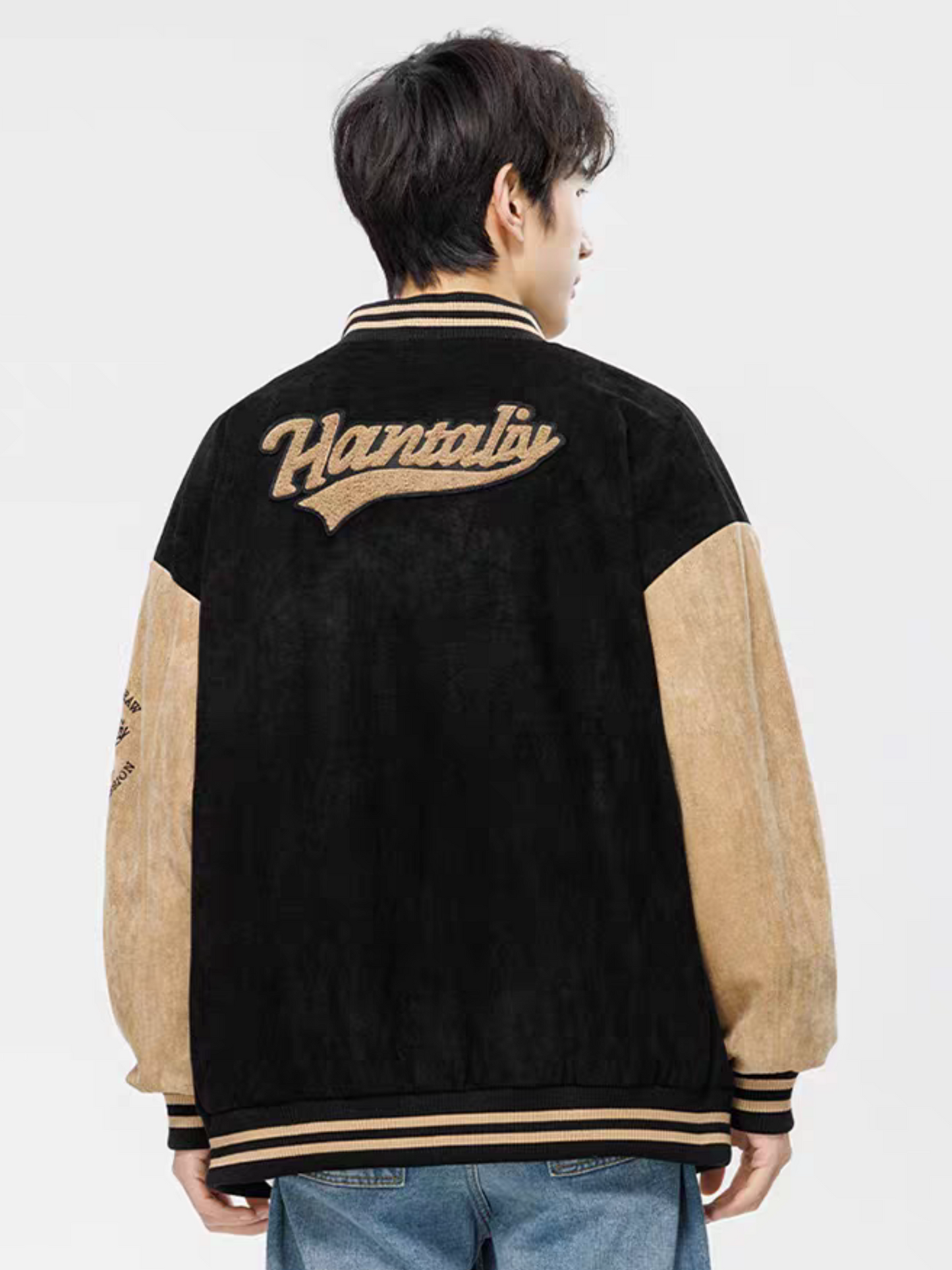 Back view of model wearing black and beige varsity jacket with chenille ''Hantaliv'' logo and striped hem