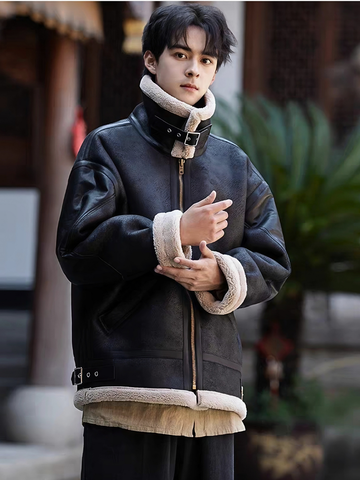 Man in black faux shearling aviator jacket with high collar and beige lining, posing outdoors in winter streetwear style