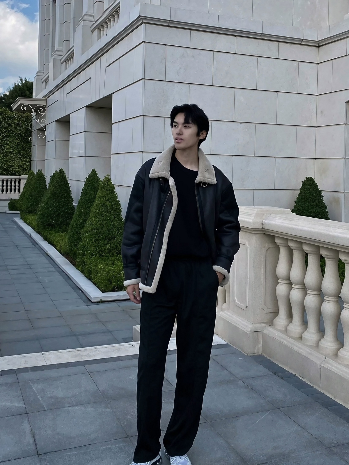 Man in black faux shearling aviator jacket with open front, winter casual outfit, standing by European-style building