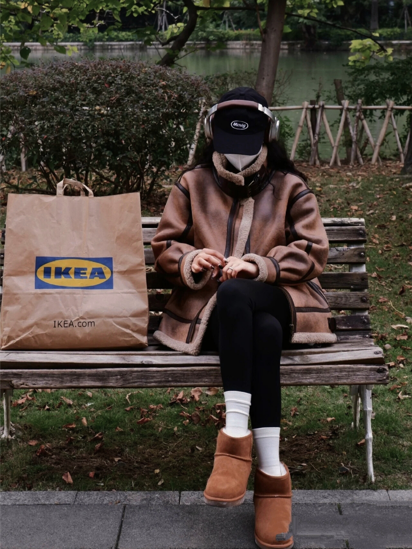 Woman in brown faux shearling aviator jacket sitting on park bench with IKEA bag and casual winter style