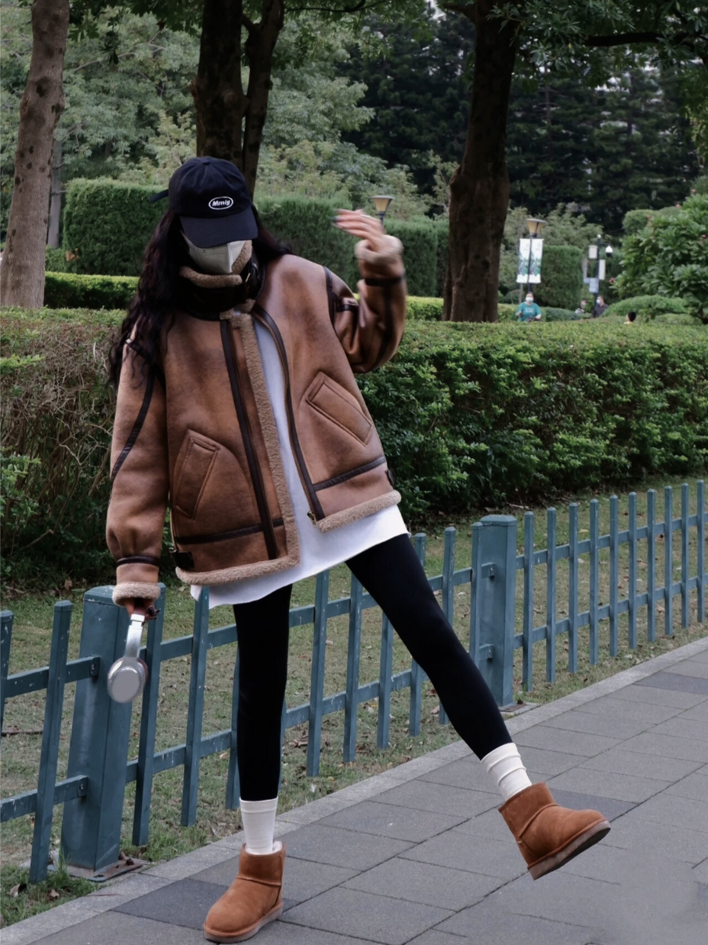 Woman wearing brown faux shearling aviator jacket making playful gesture in park streetwear look