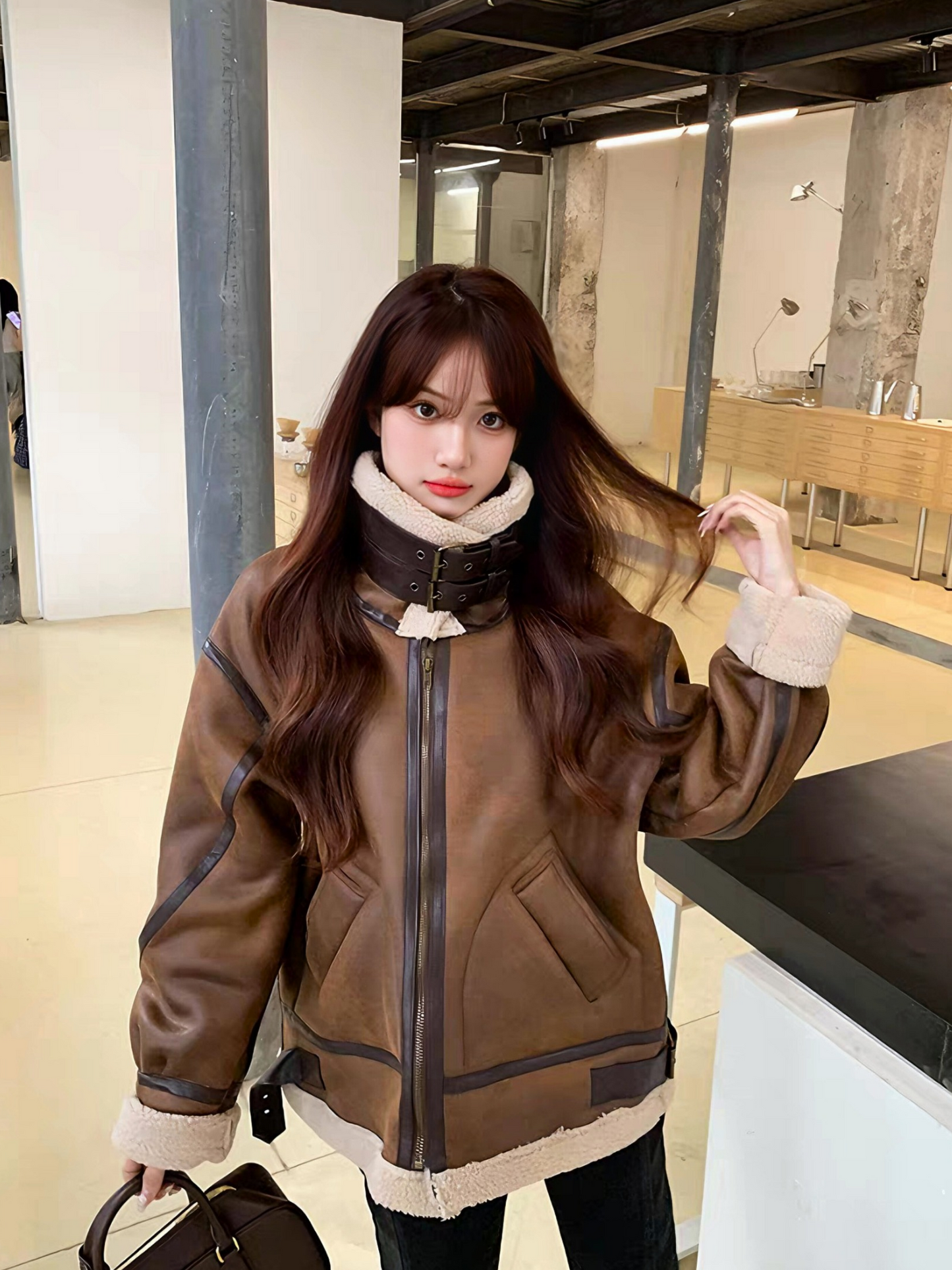 Woman wearing oversized brown faux shearling aviator jacket with high collar and buckle strap, casual streetwear look