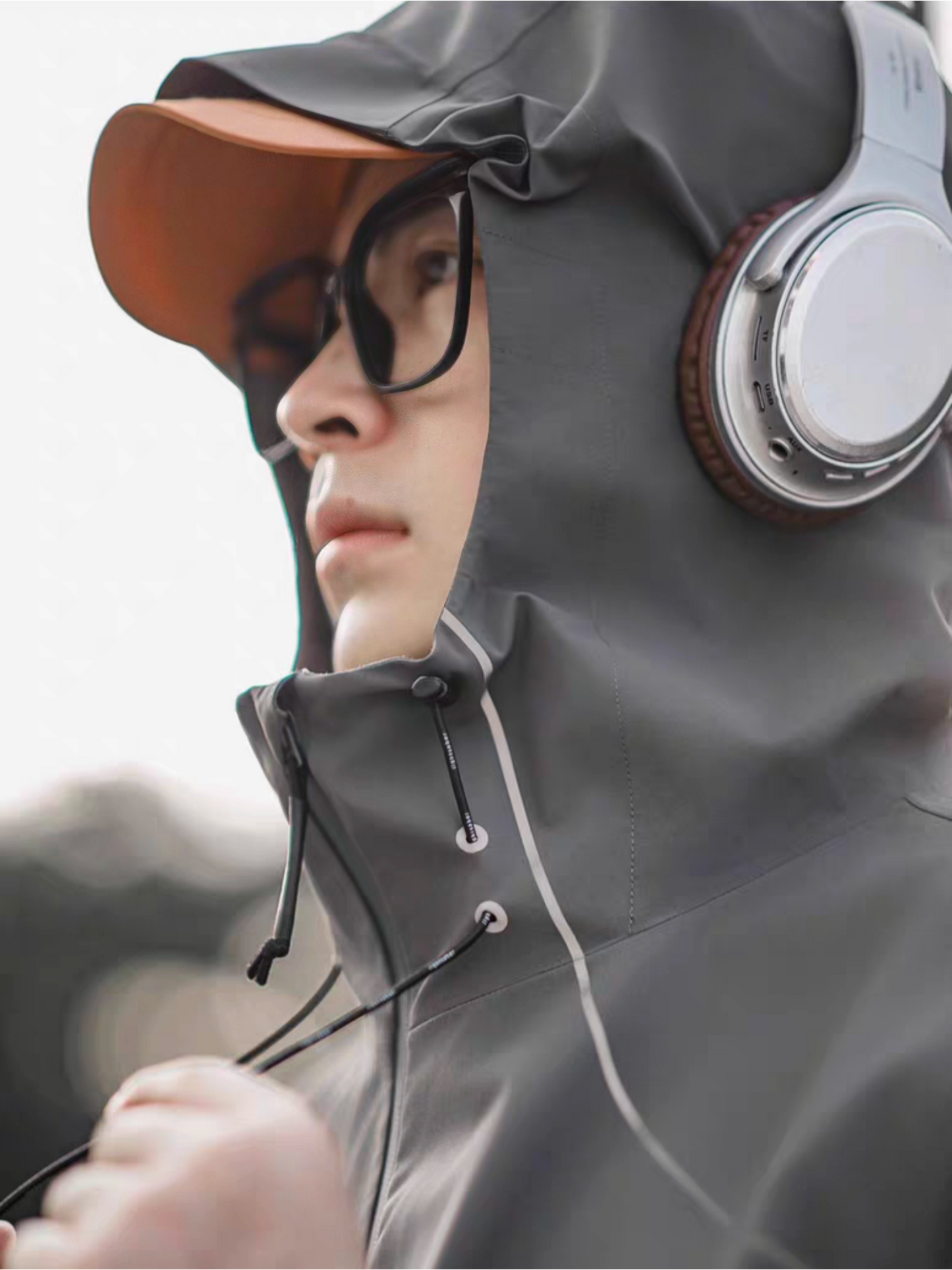 Close-up side profile of a model wearing STVLE lightsaber reflective jacket with hood up, orange cap and headphones