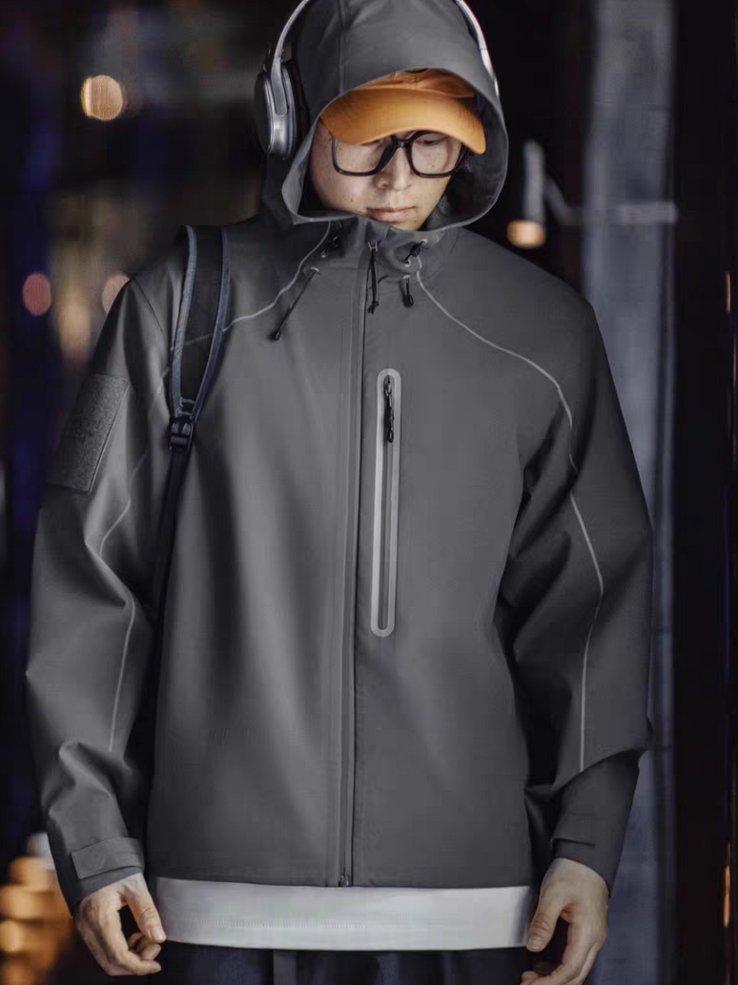 Model wearing STVLE lightsaber reflective techwear jacket with orange cap and headphones in a nighttime urban scene