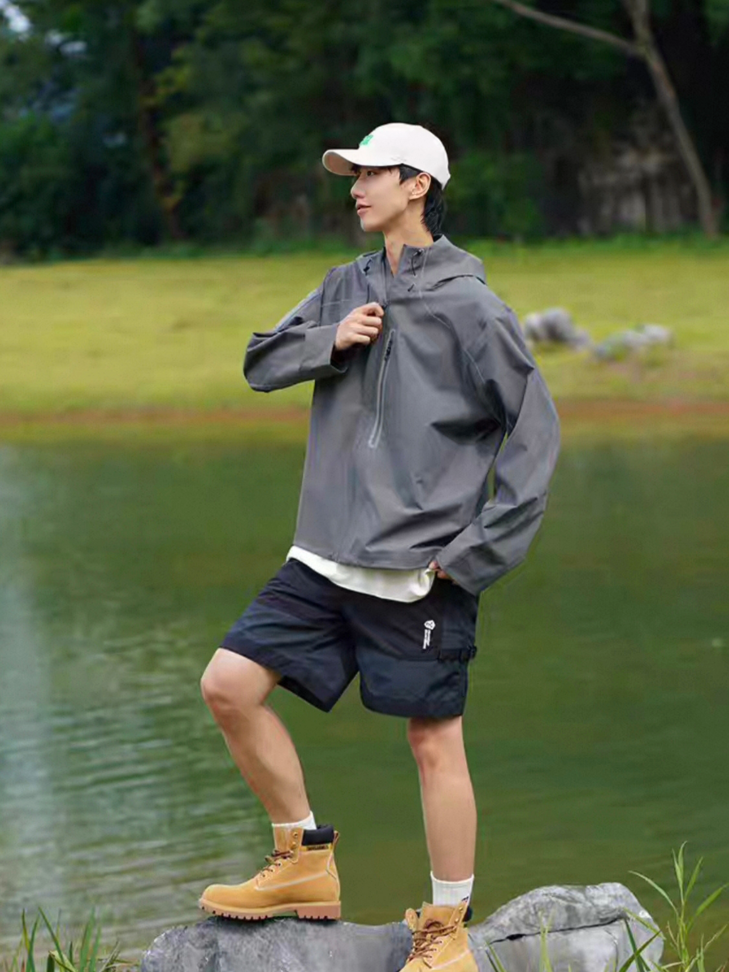 Full-body shot of model wearing STVLE lightsaber techwear jacket paired with shorts and boots, standing by a lake, showcasing outdoor adventure style and practical functionality.