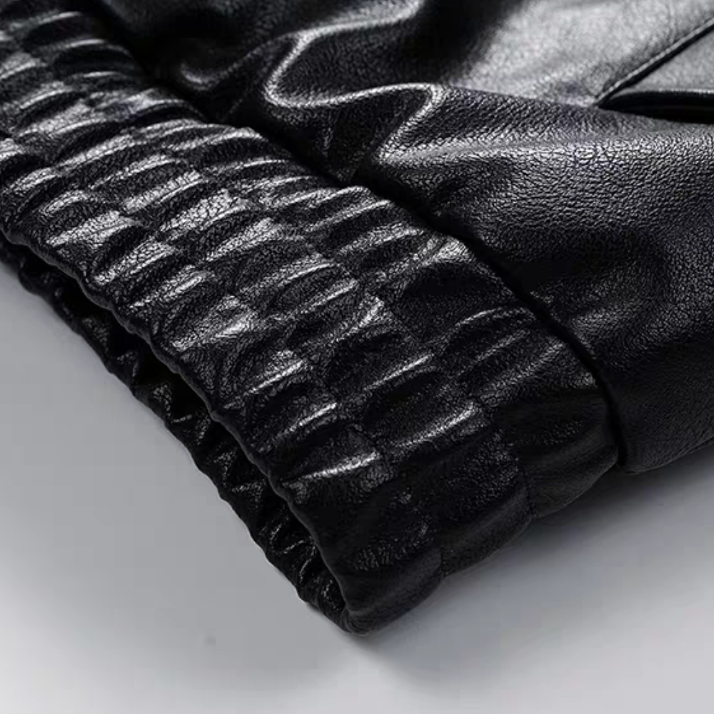 Close-up detail of elastic hem on black faux leather varsity jacket, showcasing glossy texture and wrinkle pattern