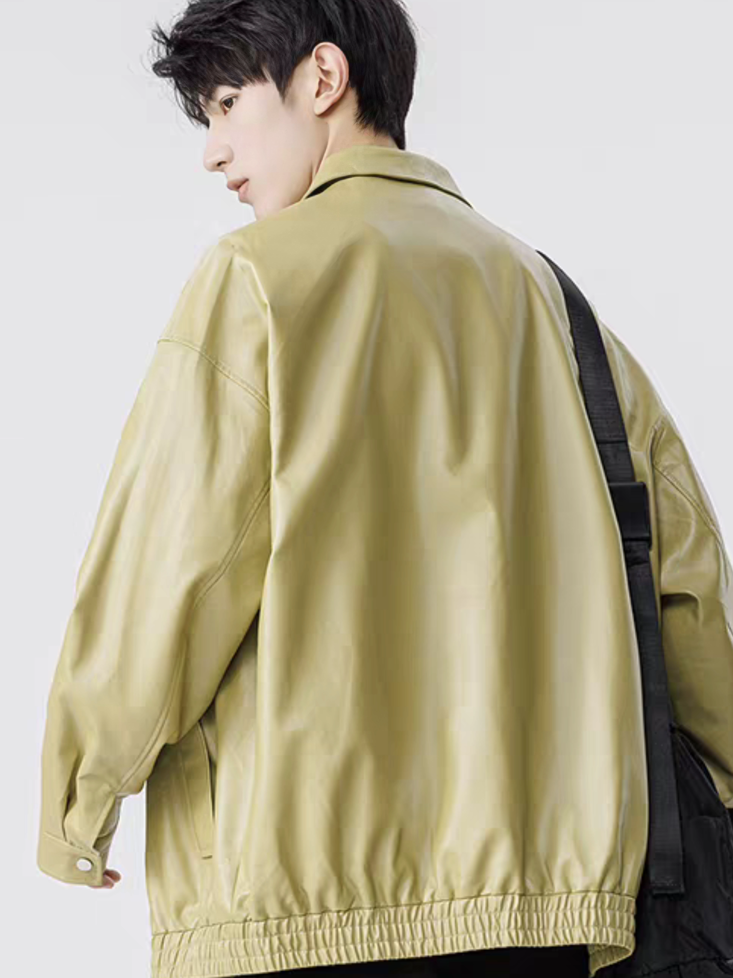 Model wearing green faux leather varsity jacket, shown from back angle with shoulder stitching and elastic hem