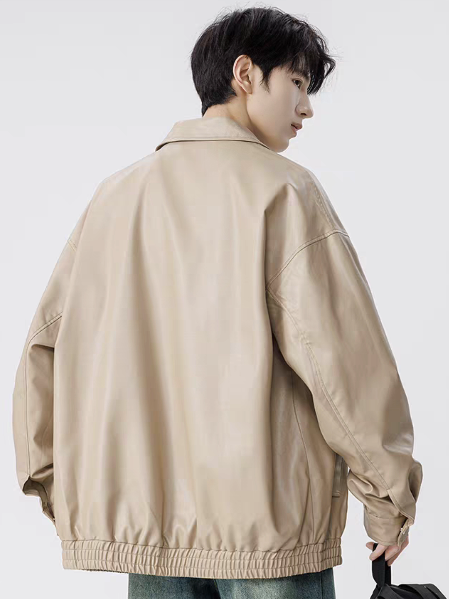 Model wearing khaki faux leather varsity jacket, shown from back angle with drop-shoulder design and elastic hem