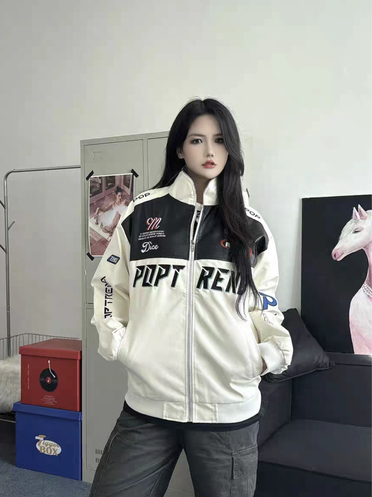 Female model wearing white racing PU leather jacket with hands in pockets, showcasing unisex streetwear style in an indoor casual setting