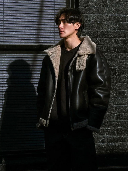 Model wearing black faux shearling aviator jacket in vegan suede, standing in dramatic sunlight and shadow for winter street style look