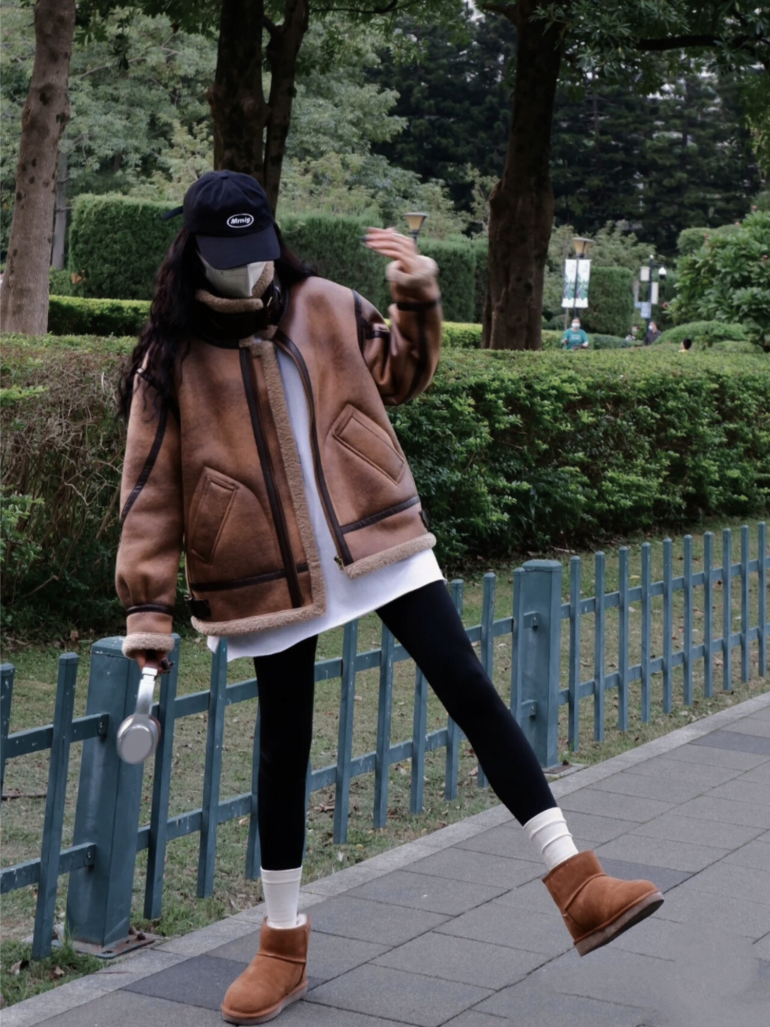 Woman wearing brown faux shearling aviator jacket making playful gesture in park streetwear look