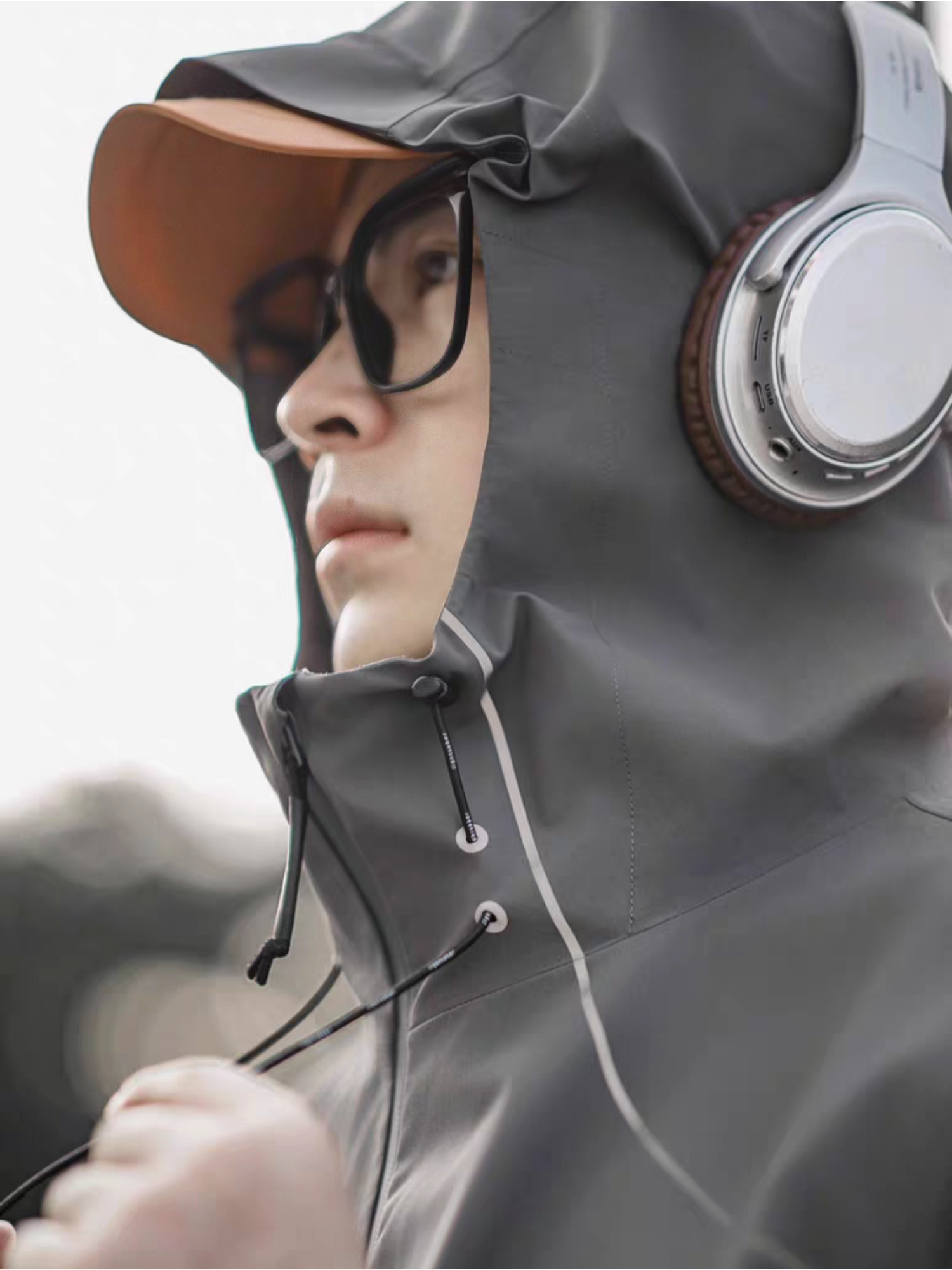 Close-up side profile of a model wearing STVLE lightsaber reflective jacket with hood up, orange cap and headphones