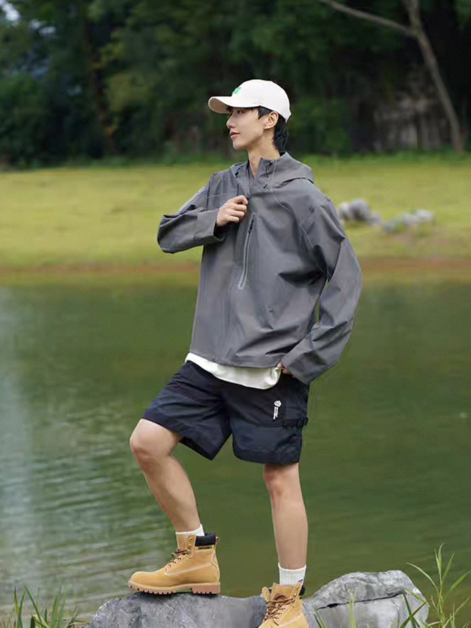 Full-body shot of model wearing STVLE lightsaber techwear jacket paired with shorts and boots, standing by a lake, showcasing outdoor adventure style and practical functionality. 